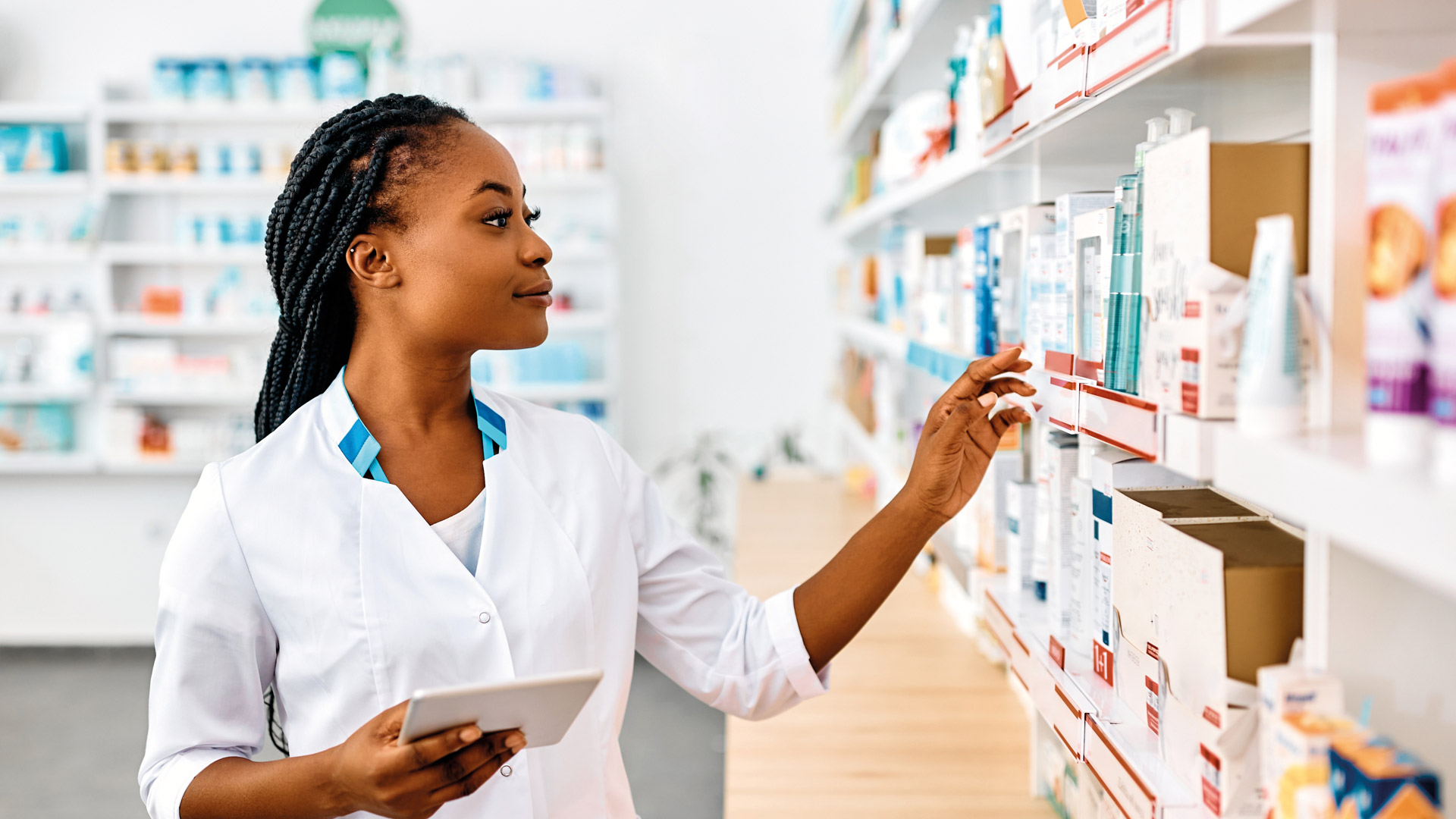 Woman working a pharmacy looking at the product shelves with a notepad